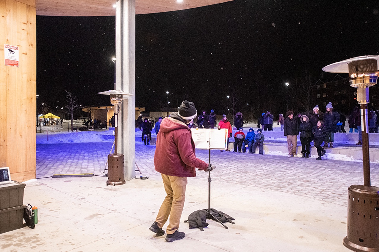 A young artist singing in front of a crowd at night in the winter
