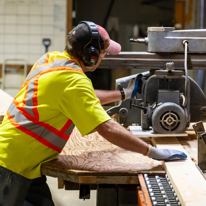 Employee at local manufacturing business, Tarpin Lumber, cutting pieces of lumber.