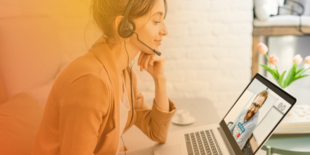 Woman with headset smiling at laptop during virtual meeting