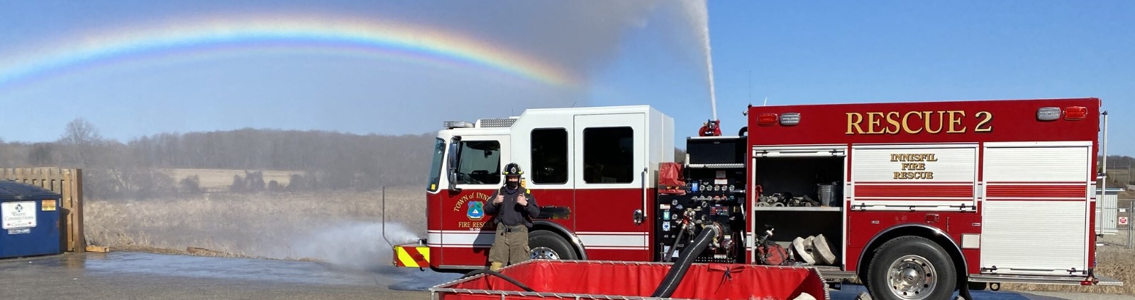 Firefighter standing in front of fire truck with rainbow in sky background