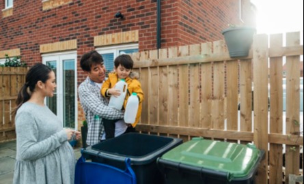 Father, daughter and grandson standing outside disposing of recycling into a bin