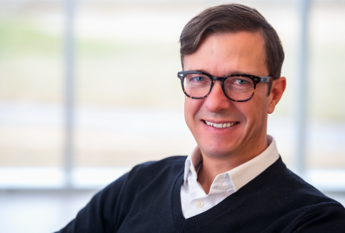 White man wearing glasses smiling in headshot