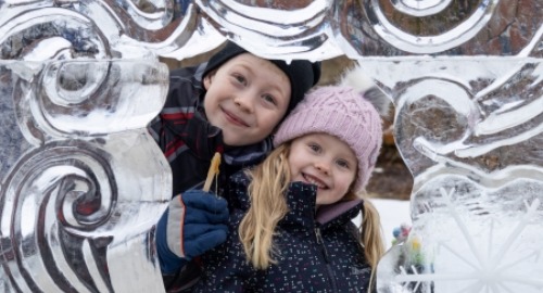 Two kids smiling behind ice sculpture 