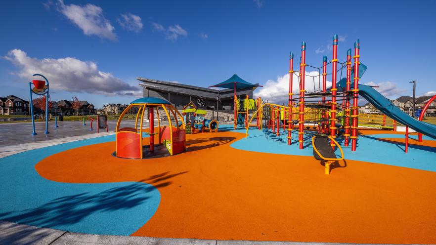 Inclusive playground at Margaretta Park featuring a climbing structure, slide, spinner, and accessible play equipment on colourful rubber safety surfacing.