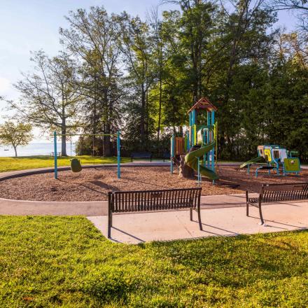 a park play ground with two benches surrounded by trees and grass